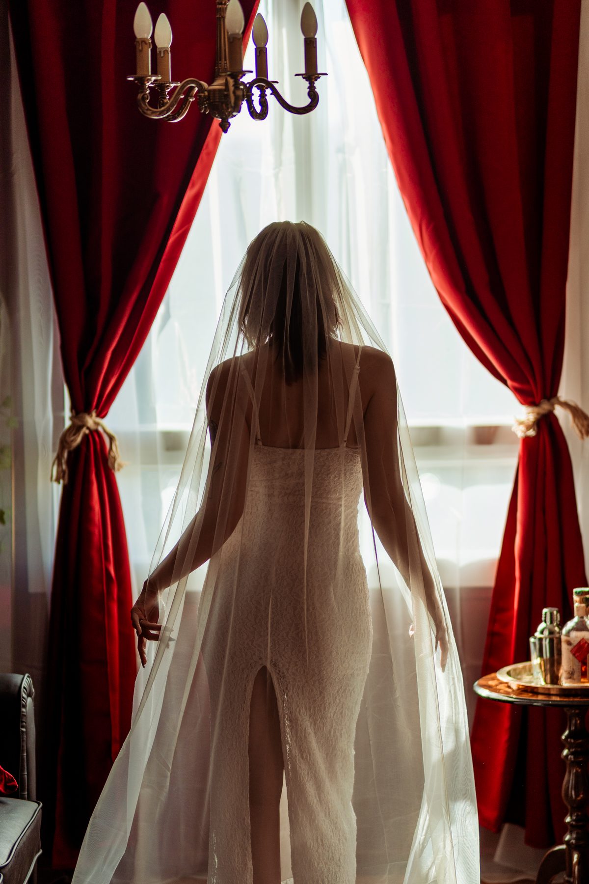 Mariée de dos devant des rideaux rouges, voile déployé